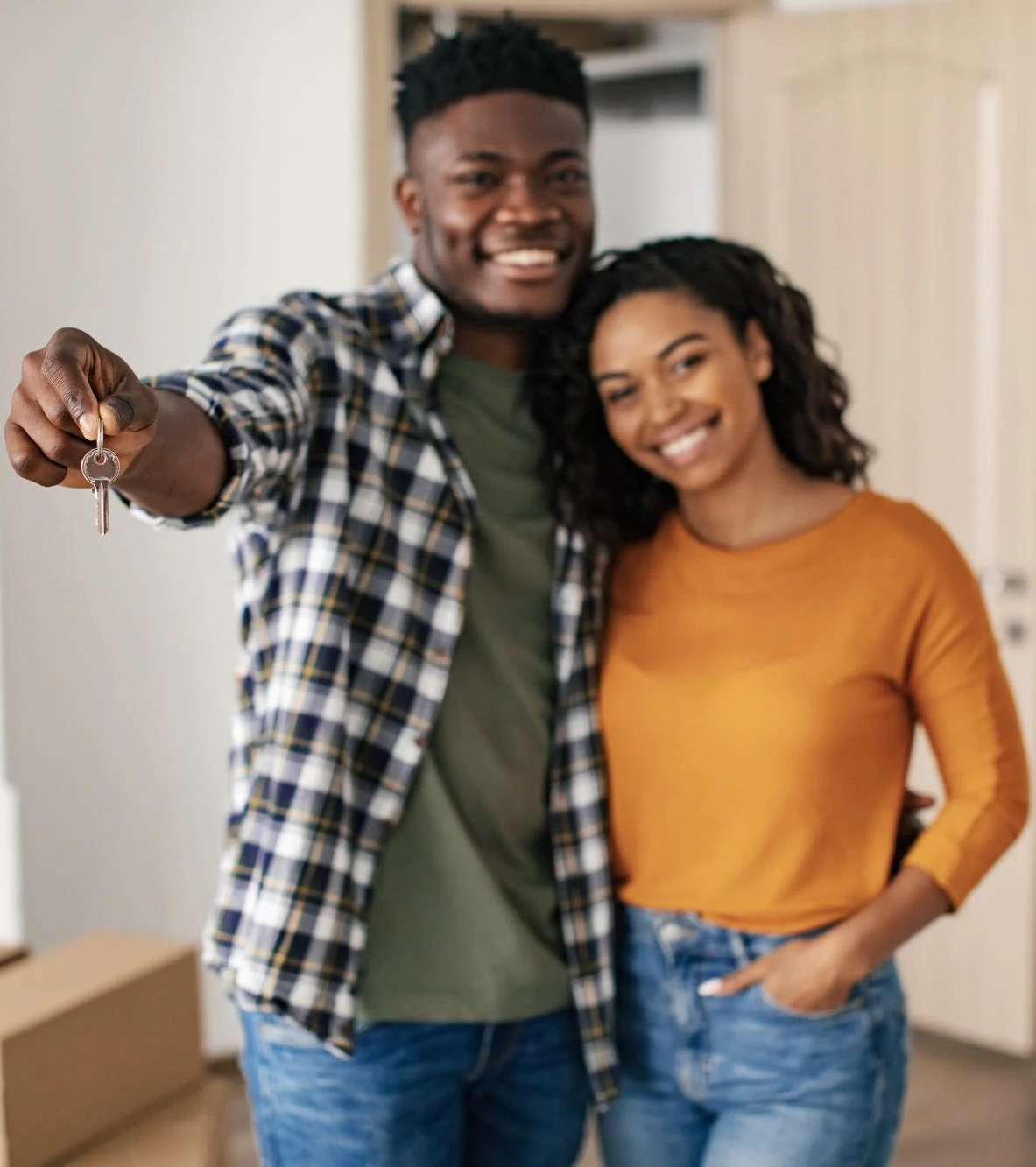 A young couple smiling and holding a key in front of their new home, symbolizing their excitement and achievement.